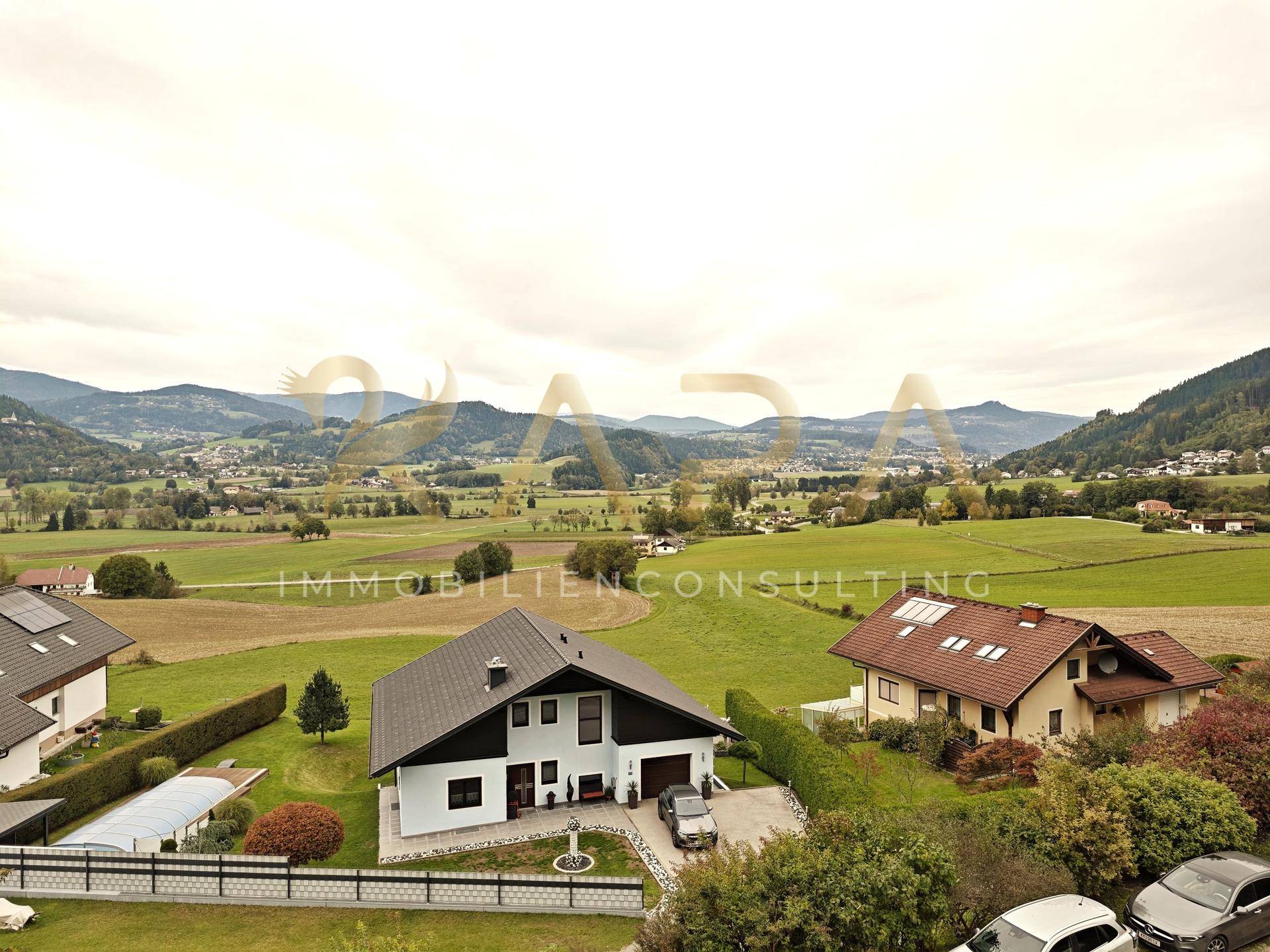 Luftaufnahme von Einfamilienhäusern in einer grünen, hügeligen Landschaft mit Bergblick.