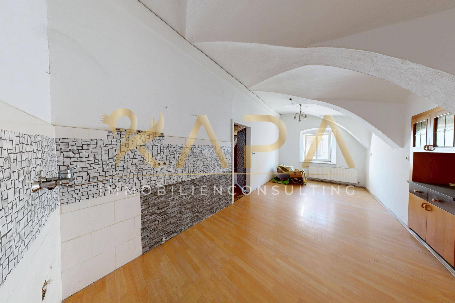 Offener Wohnbereich mit Gewölbedecke, Holzboden und vorbereiteter Küchenzeile.