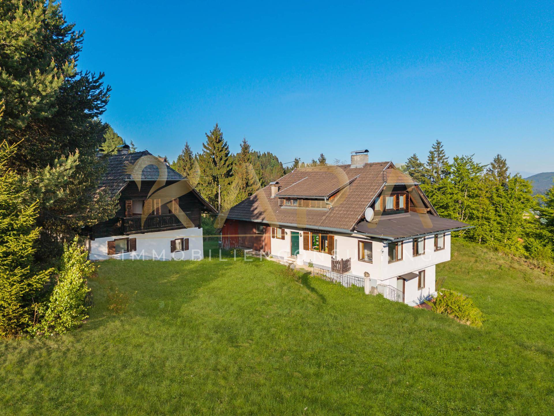 Drohnenaufnahme der beiden Gebäude auf dem Grundstück, eingebettet in die grüne Hügellandschaft.