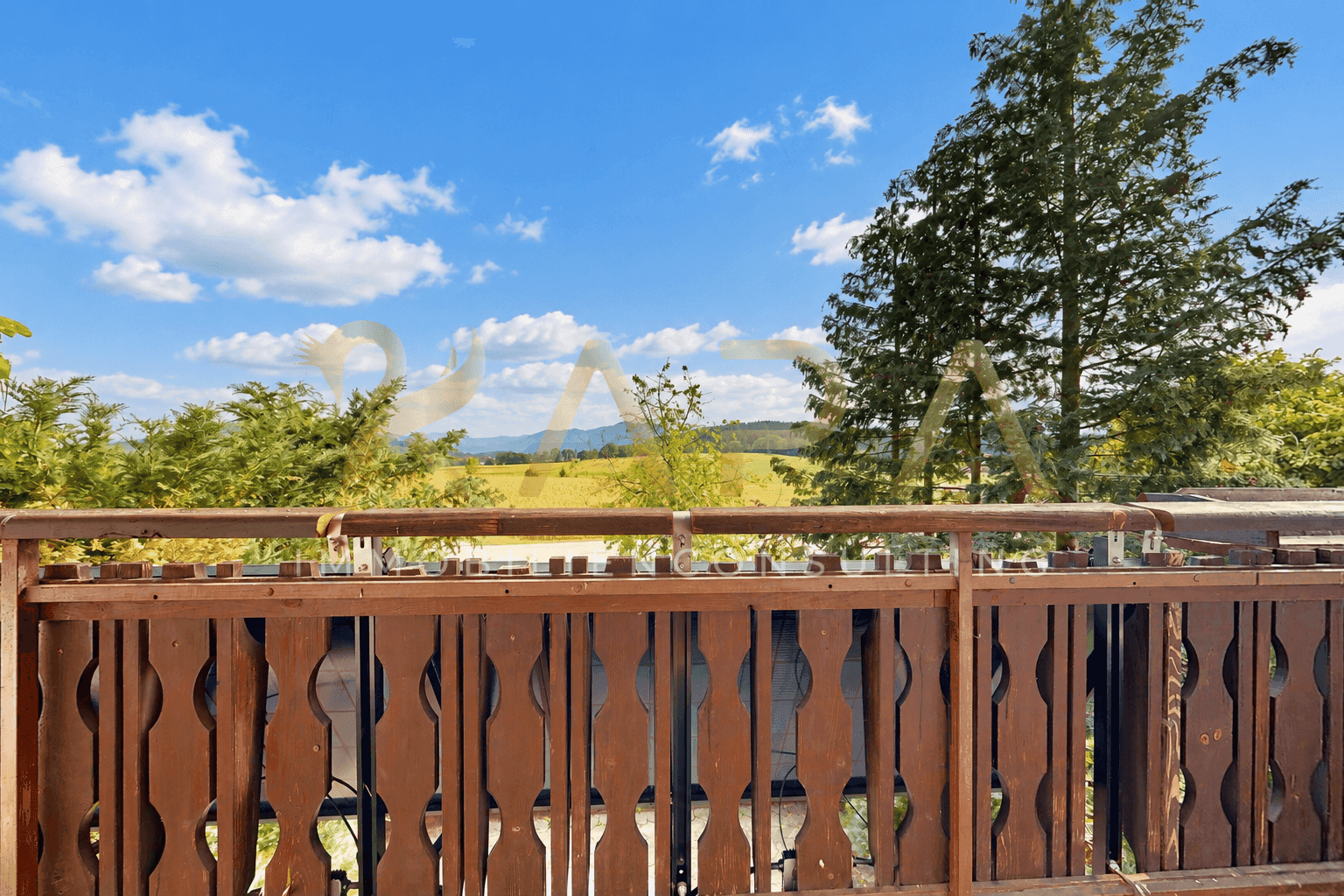 Holzbalkon mit geschnitztem Geländer und weitem Blick auf die grüne Landschaft.