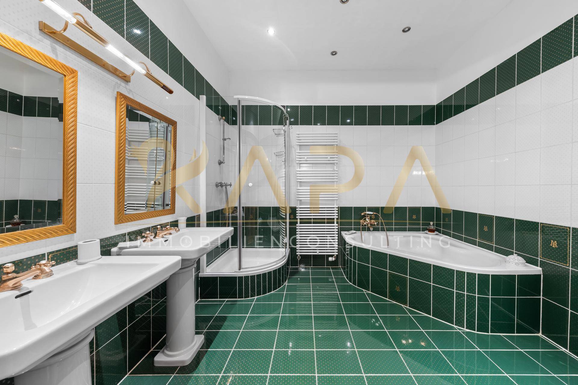 Geräumiges Badezimmer mit grünen und weißen Fliesen, Doppelwaschbecken, Dusche und Badewanne, klassisch gestaltet.