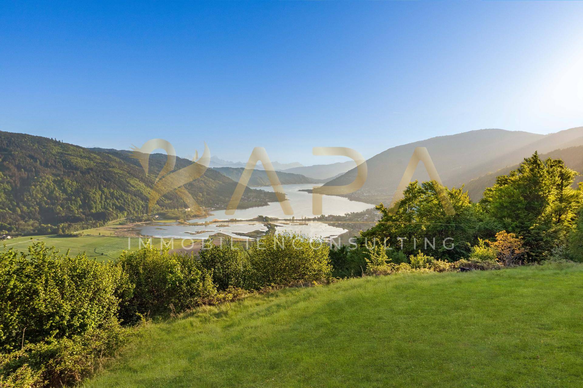 Malerische Aussicht auf die weite grüne Landschaft mit See und Bergen unter blauem Himmel.