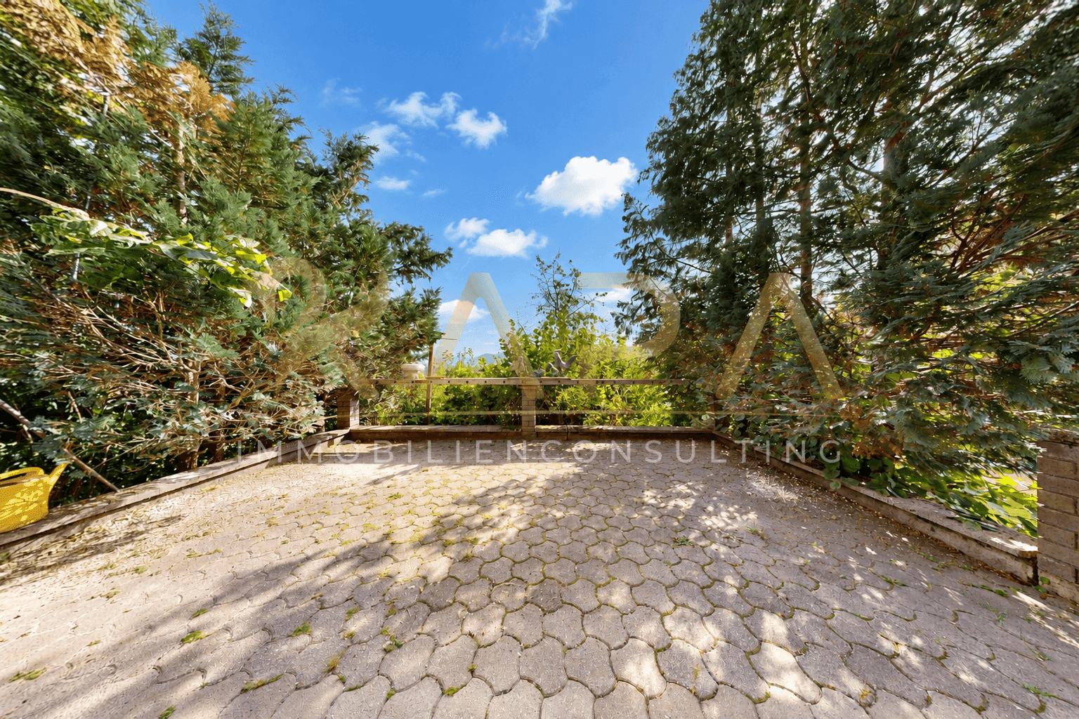 Gepflasterte Terrasse umgeben von Bäumen mit Blick auf die Landschaft.