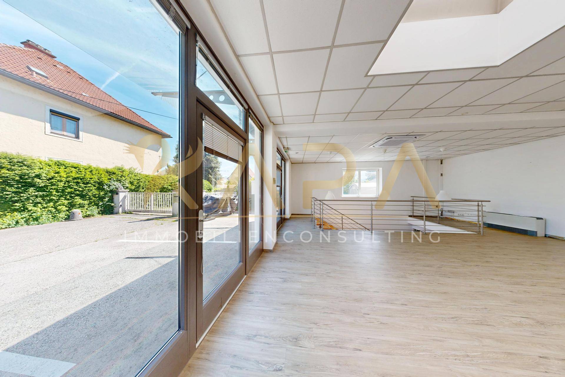 Heller Büroraum mit großen Fensterfronten, die viel Tageslicht hereinlassen und einen Blick nach draußen bieten.