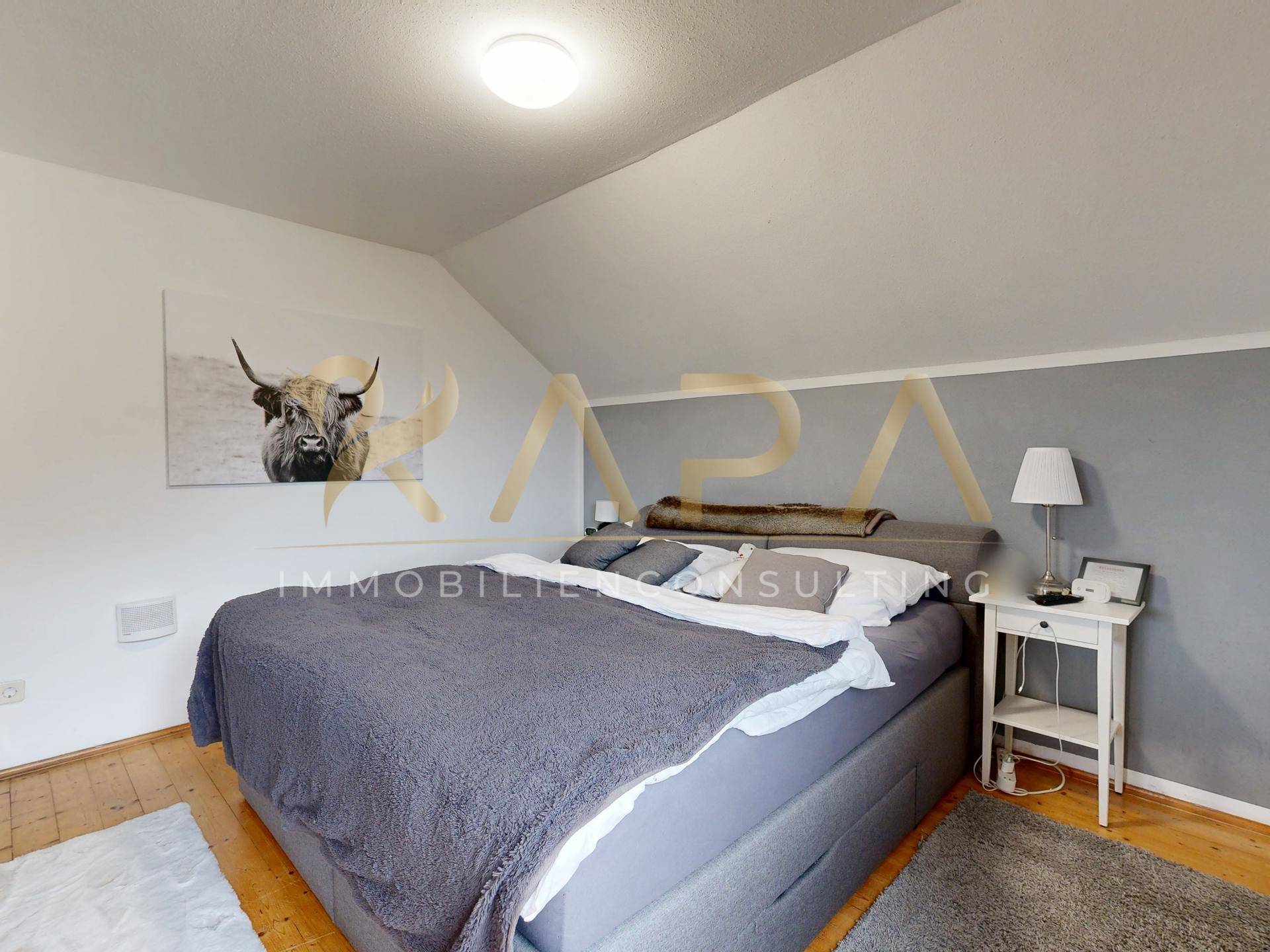 Schlafzimmer im Dachgeschoss mit großem Bett, Holzboden und schrägen Wänden, bietet viel Gemütlichkeit.