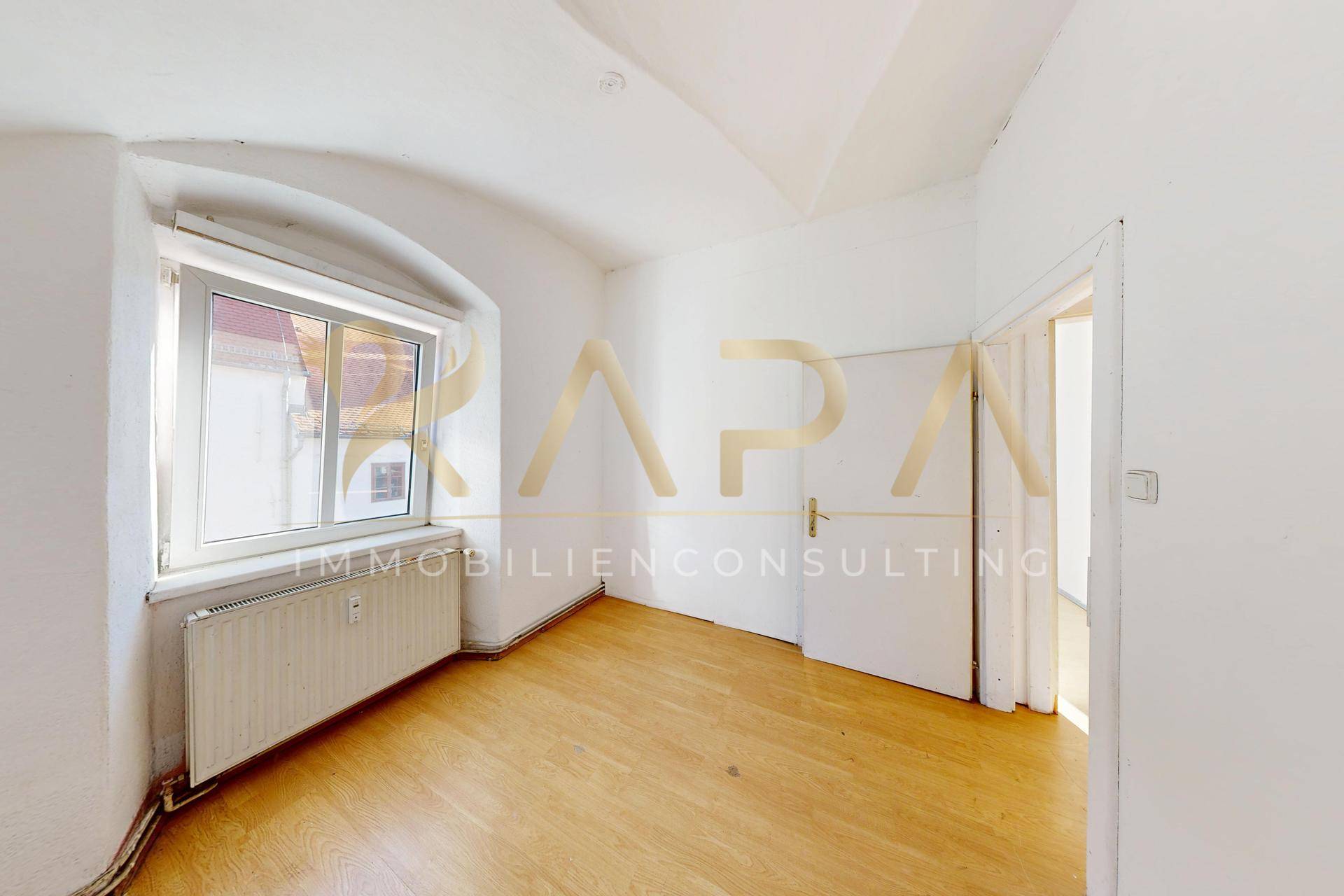 Helles Zimmer mit Holzboden, weiß gestrichenen Wänden und einem Fenster.