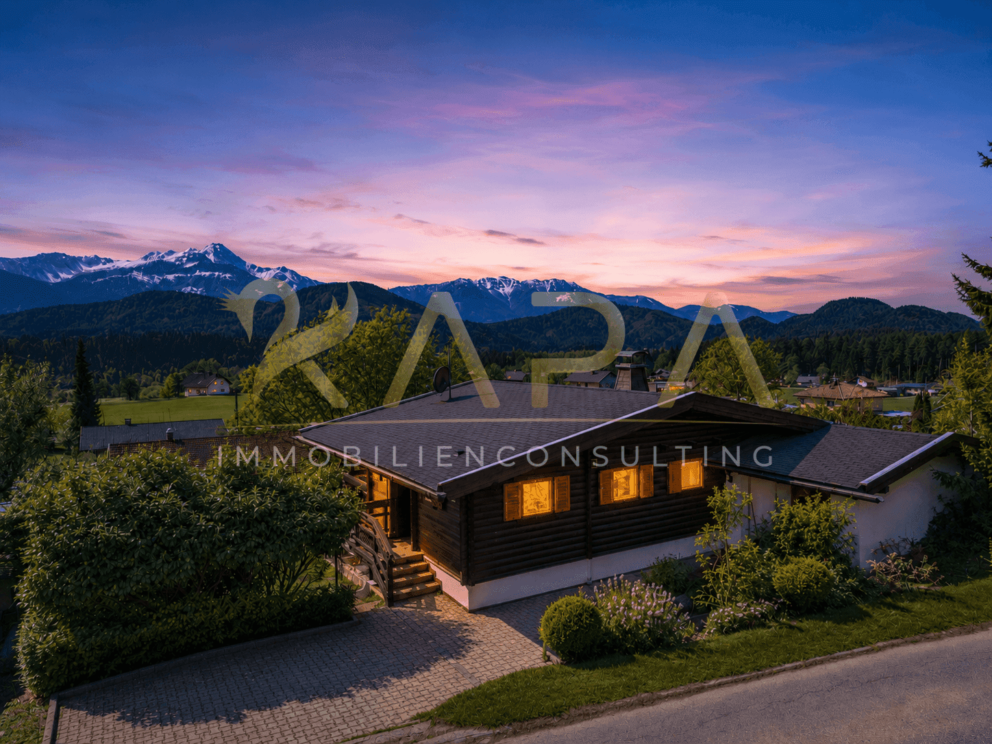 Holzhaus bei Sonnenuntergang mit beleuchteten Fenstern und majestätischem Bergblick.