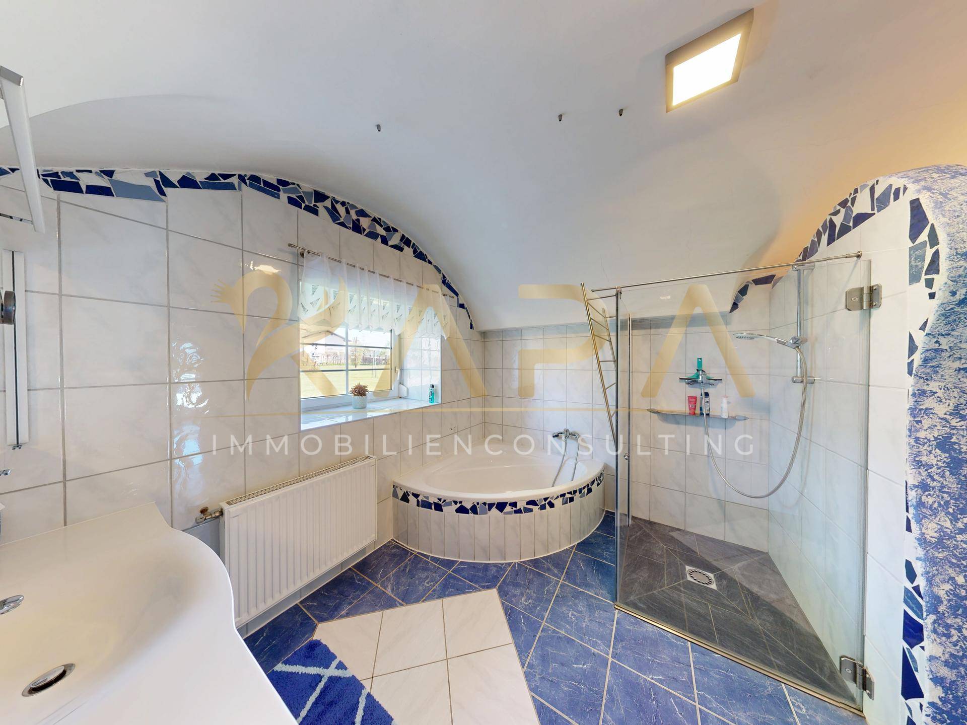 Badezimmer mit blauen und weißen Fliesen, Eckbadewanne, begehbarer Dusche und Fenster.