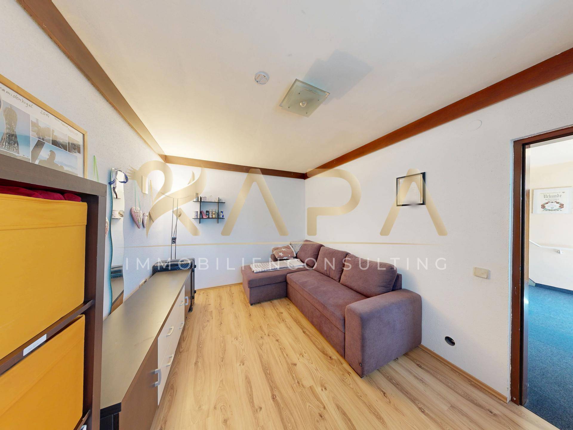 Kleiner Raum mit Sofa, Regalen und Laminatboden, ideal als Gästezimmer oder Büro.