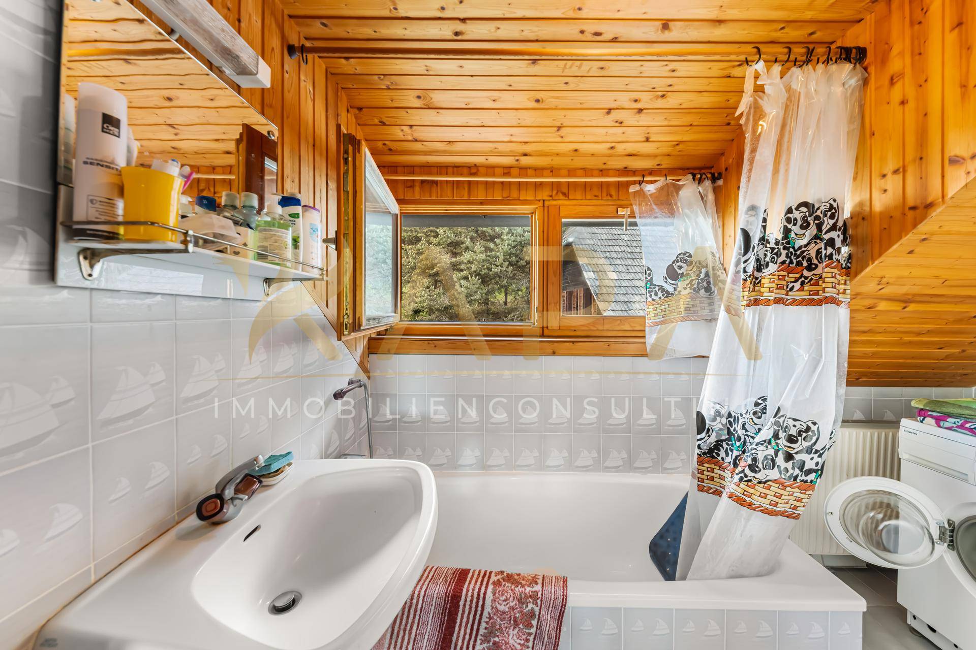 Badezimmer mit Holzverkleidung an Decke und Wänden, Badewanne und Fenster mit Waldblick.