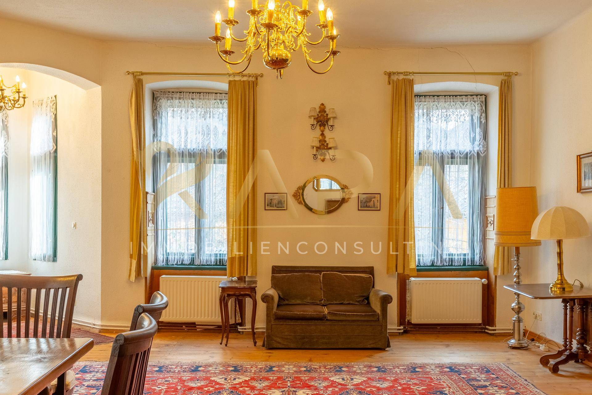 Geräumiger Wohn- und Essbereich mit hohen Decken, Holzboden und einem opulenten Kronleuchter.