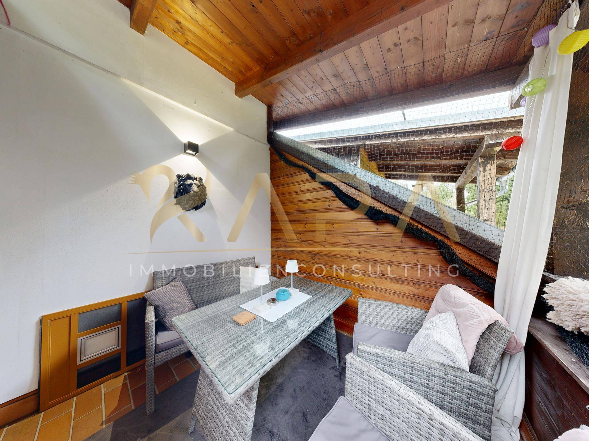 Überdachter Balkon mit Rattanmöbeln und Holzwänden, ideal für entspannte Stunden im Freien.