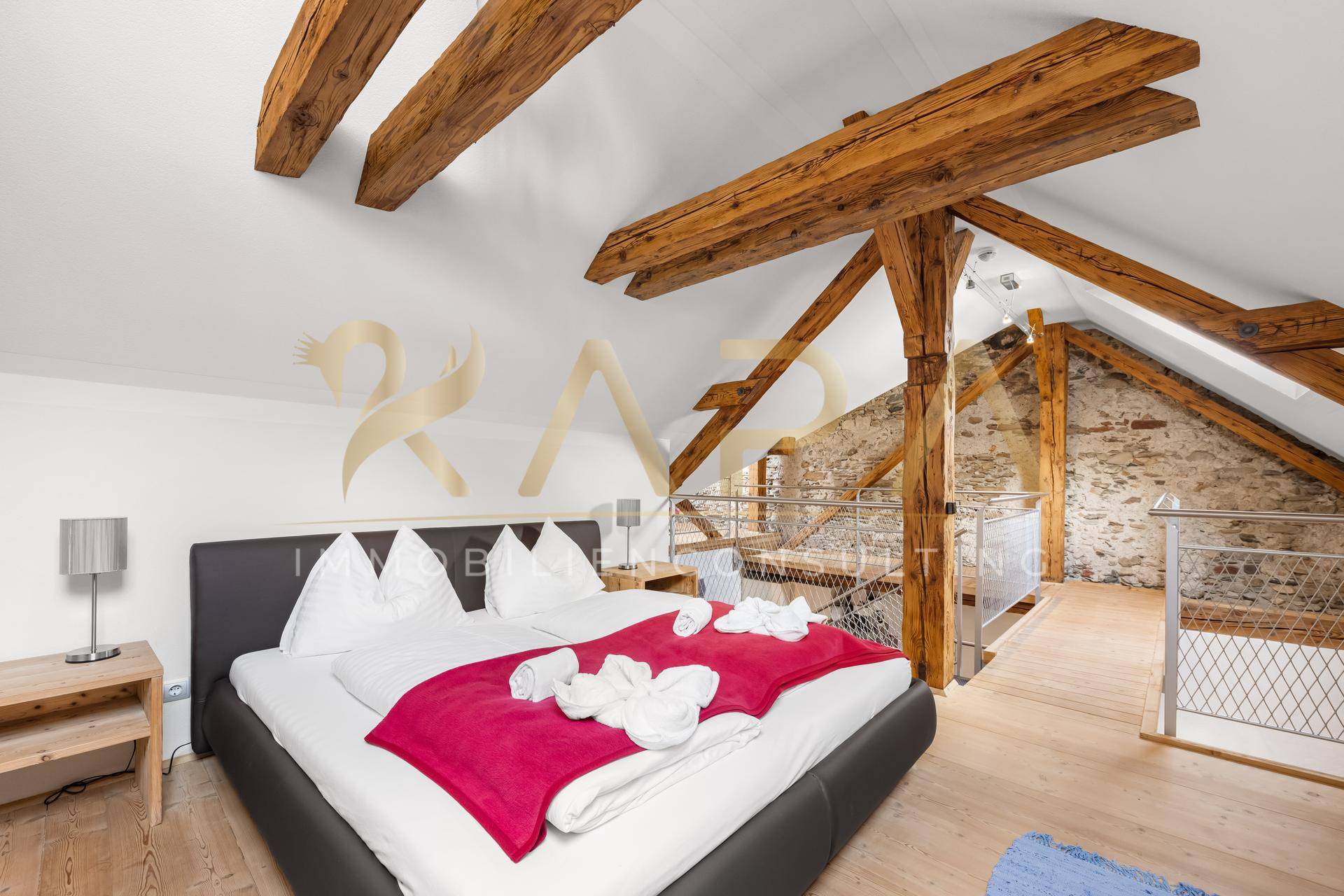 Gemütliches Schlafzimmer im Dachgeschoss mit sichtbaren Holzbalken und Holzboden.