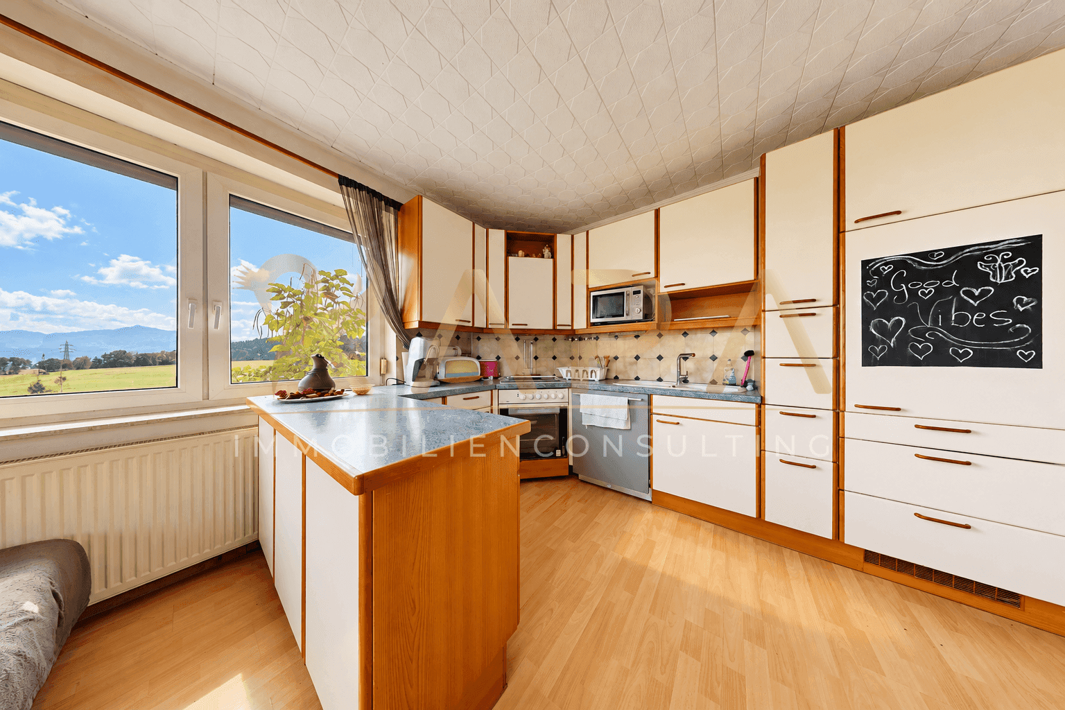 Helle Küche mit weißen und holzfarbenen Schränken, Kücheninsel und weitem Ausblick.