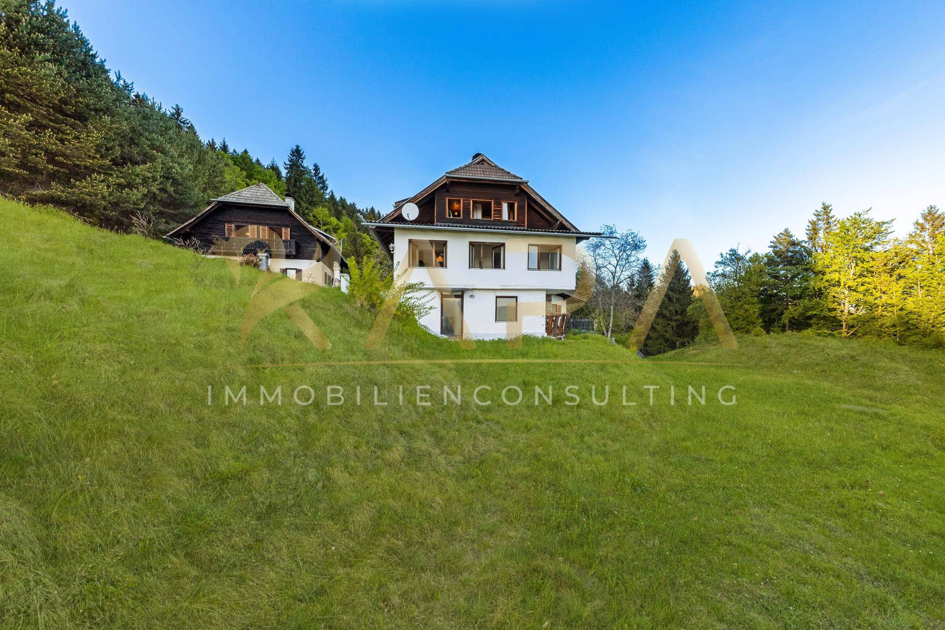 Ansicht des traditionellen Hauses auf einem sonnigen Hügel, umgeben von grünen Wiesen und Bäumen.