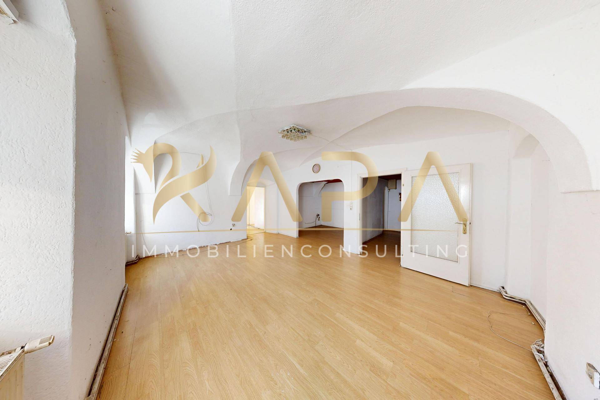 Geräumiger Wohnbereich mit eleganten Gewölbedecken, Holzboden und mehreren Türen.