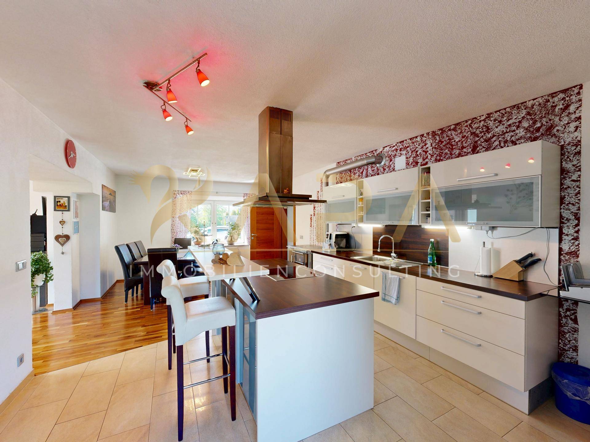 Moderne Küche mit Kochinsel, weißen Schränken und Essbereich im Hintergrund, mit Fliesen- und Holzboden.