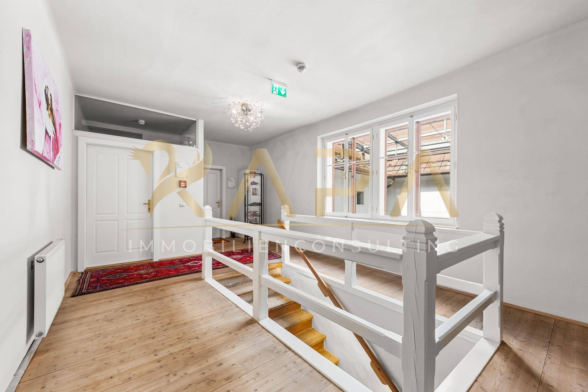 Heller Flur im Obergeschoss mit Holztreppe, Holzboden und Fenstern zum Innenhof.