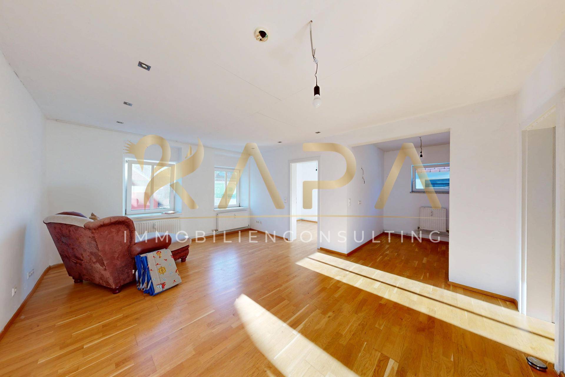 Heller Wohnbereich mit Holzboden, großzügigen Fenstern und einem Sessel.