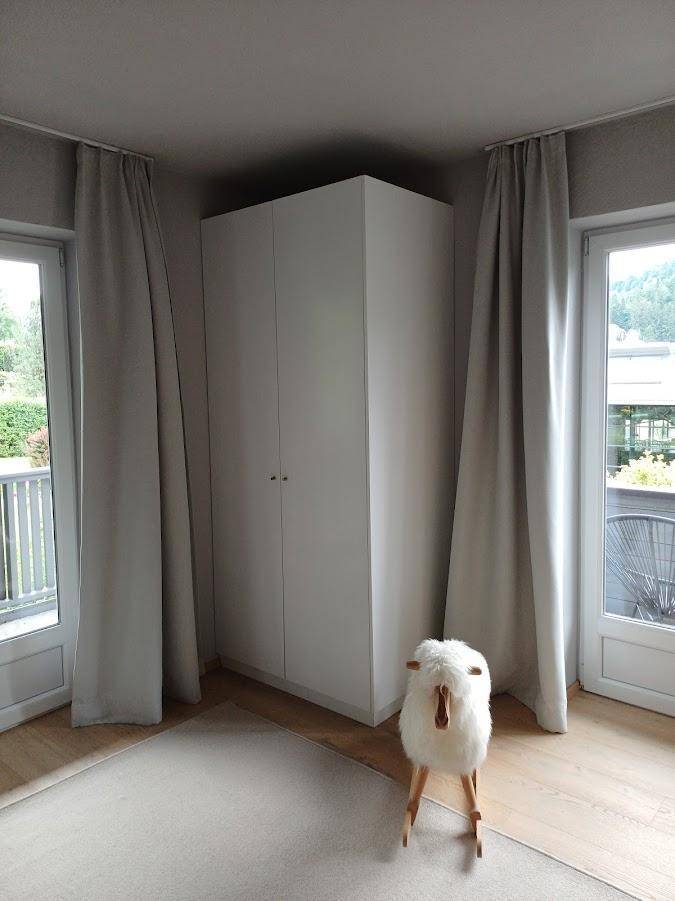 Helles Schlafzimmer mit weißem Kleiderschrank und großen Fenstern zum Außenbereich.