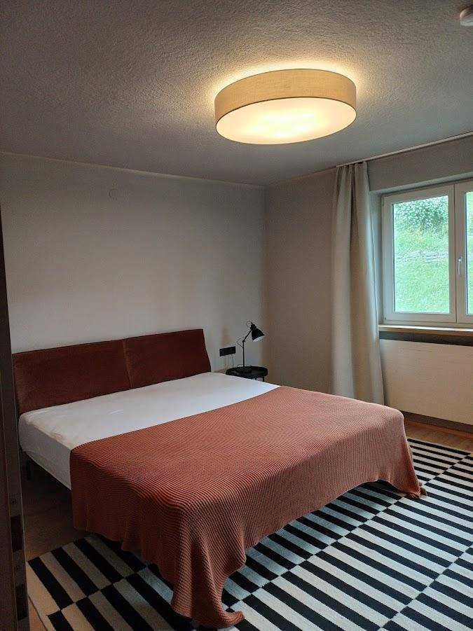 Gemütliches Schlafzimmer mit Doppelbett, Holzboden und Fenster mit Blick ins Grüne.