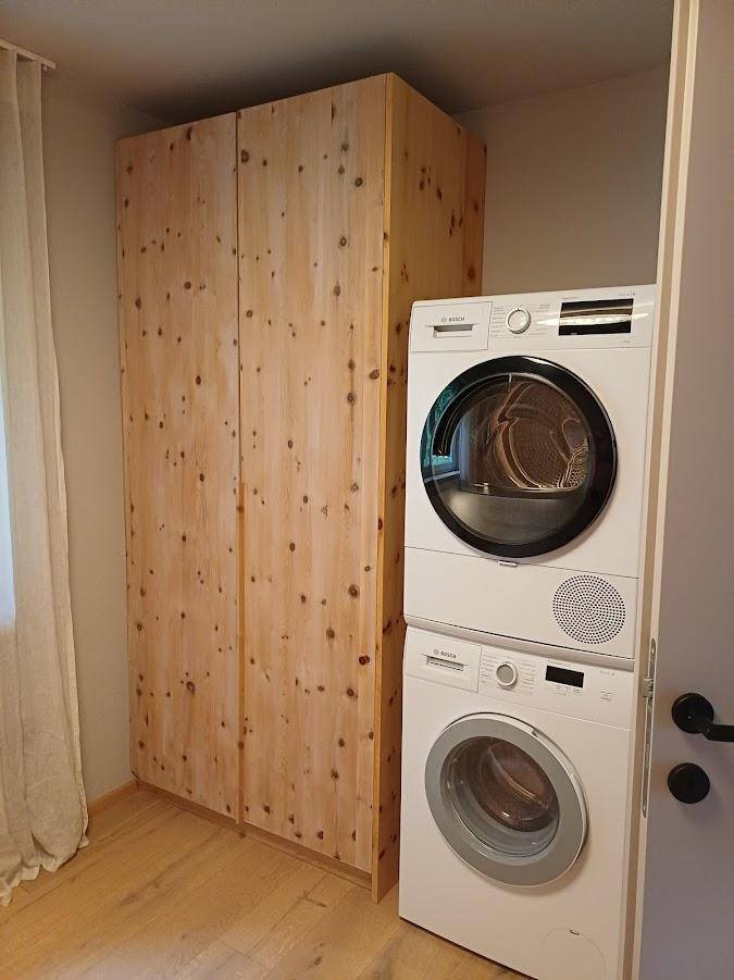 Praktischer Hauswirtschaftsraum mit gestapelter Waschmaschine und Trockner neben einem Holzschrank.