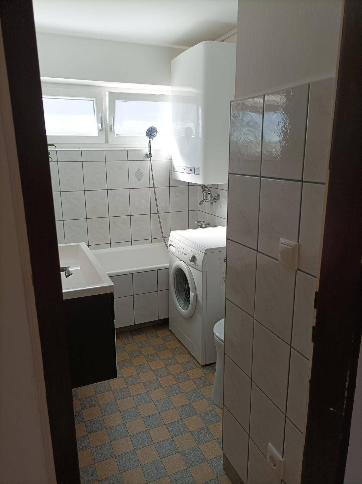 Funktionales Badezimmer mit Badewanne, Waschmaschine, gefliesten Wänden und Fenster.