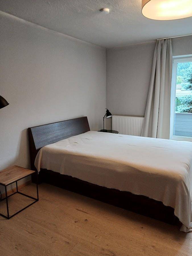 Helles Schlafzimmer mit Doppelbett, Holzboden und Zugang zu einem Balkon oder Terrasse.