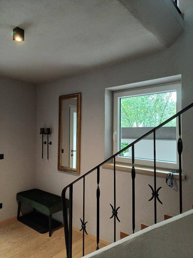 Heller Treppenaufgang mit Holzstufen, schmiedeeisernem Geländer und einem Fenster mit Blick ins Grüne.