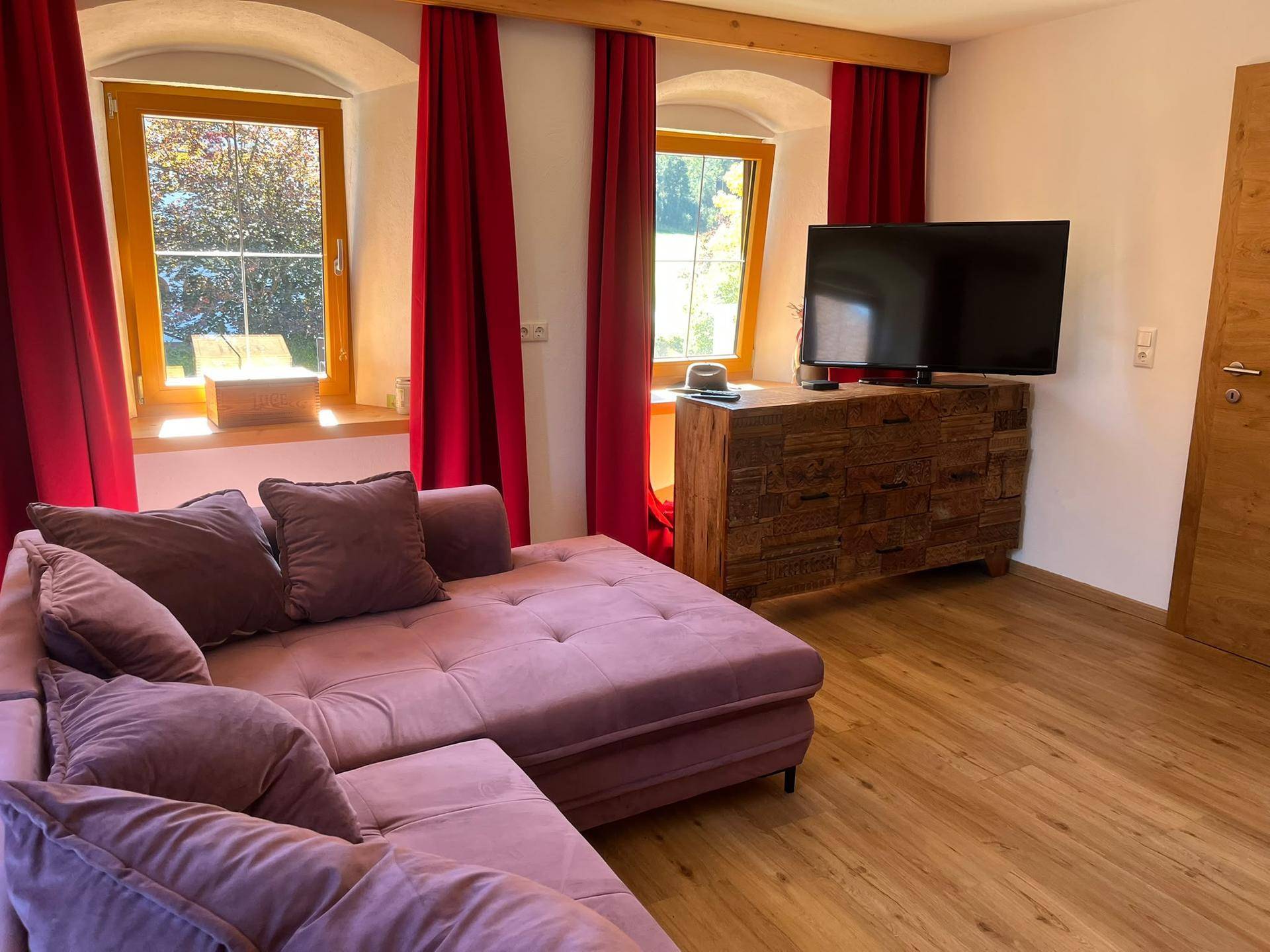 Wohnbereich mit bequemer Couch, Fernseher und rustikalen Holzbalken an der Decke.