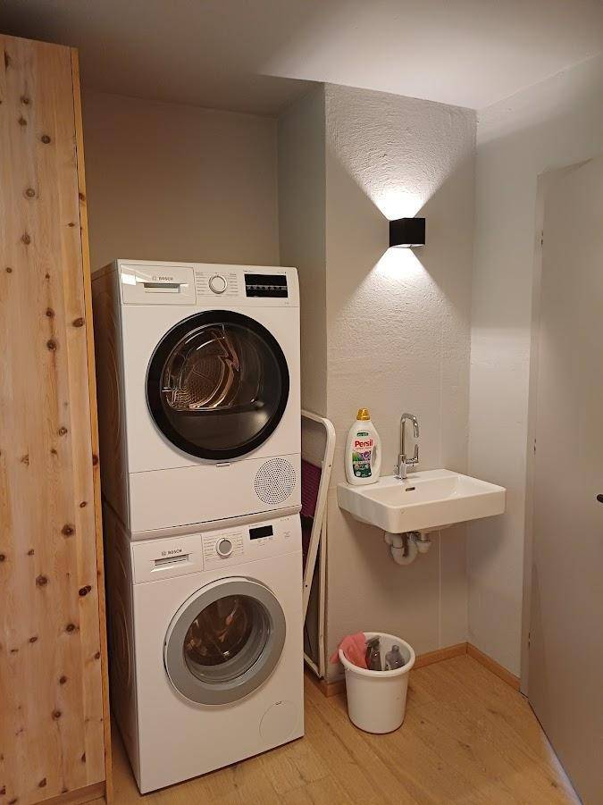 Funktionaler Hauswirtschaftsraum mit Waschmaschine, Trockner, kleinem Waschbecken und Holzschrank.