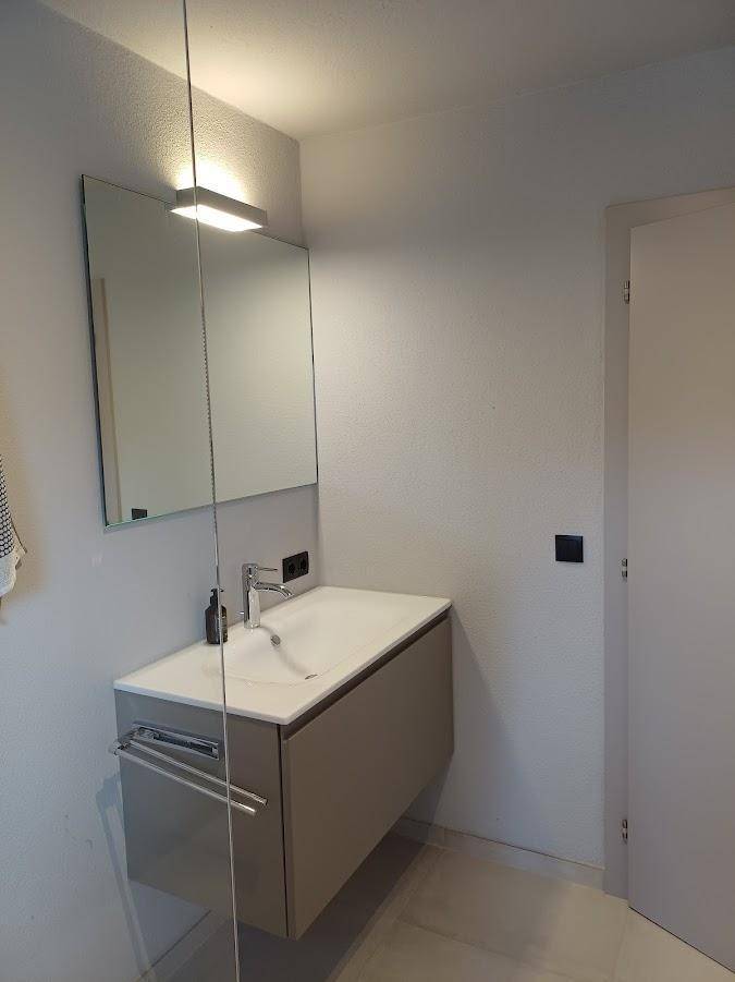 Modernes Badezimmer mit schwebendem Waschtisch, großem Spiegel und indirekter Beleuchtung.