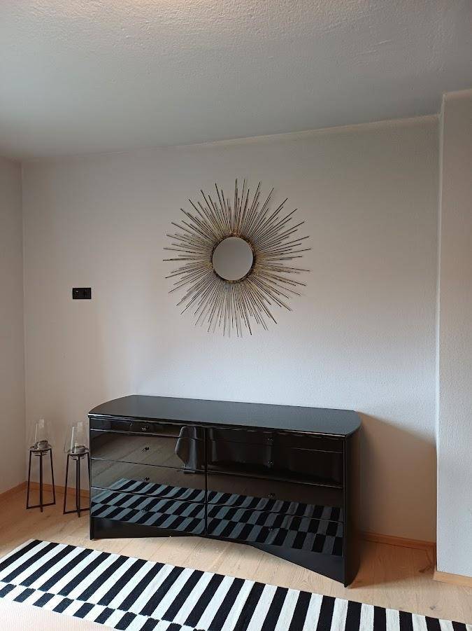 Schlafzimmer mit modernem schwarzen Sideboard, dekorativem Spiegel und Holzboden.