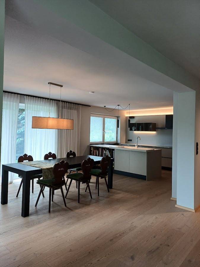 Offener Wohn-Essbereich mit Holzboden und moderner Küche im Hintergrund, ideal für geselliges Beisammensein.