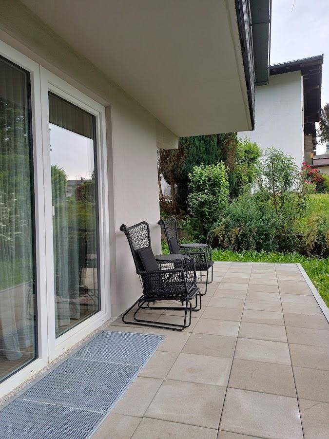 Gepflasterte Terrasse im Erdgeschoss mit zwei schwarzen Outdoor-Stühlen und Zugang zum Garten.