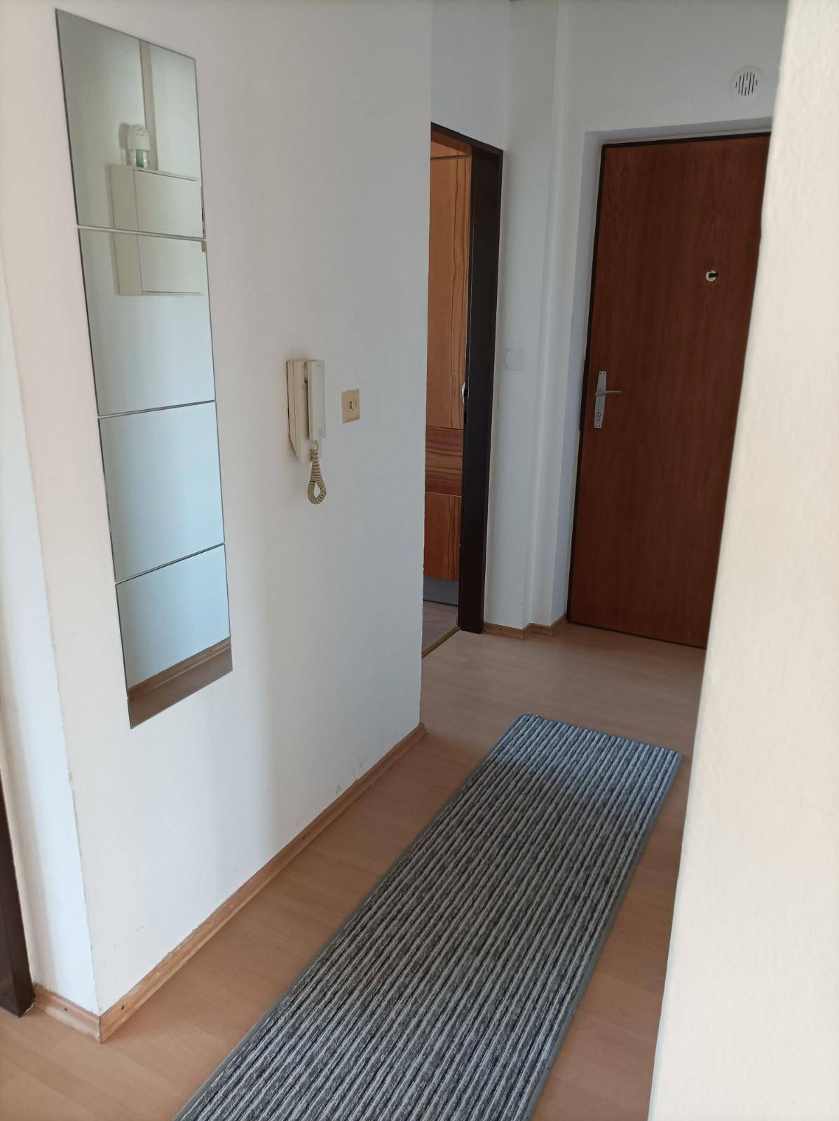 Heller Flur mit Laminatboden, Spiegel und Gegensprechanlage am Eingangsbereich.