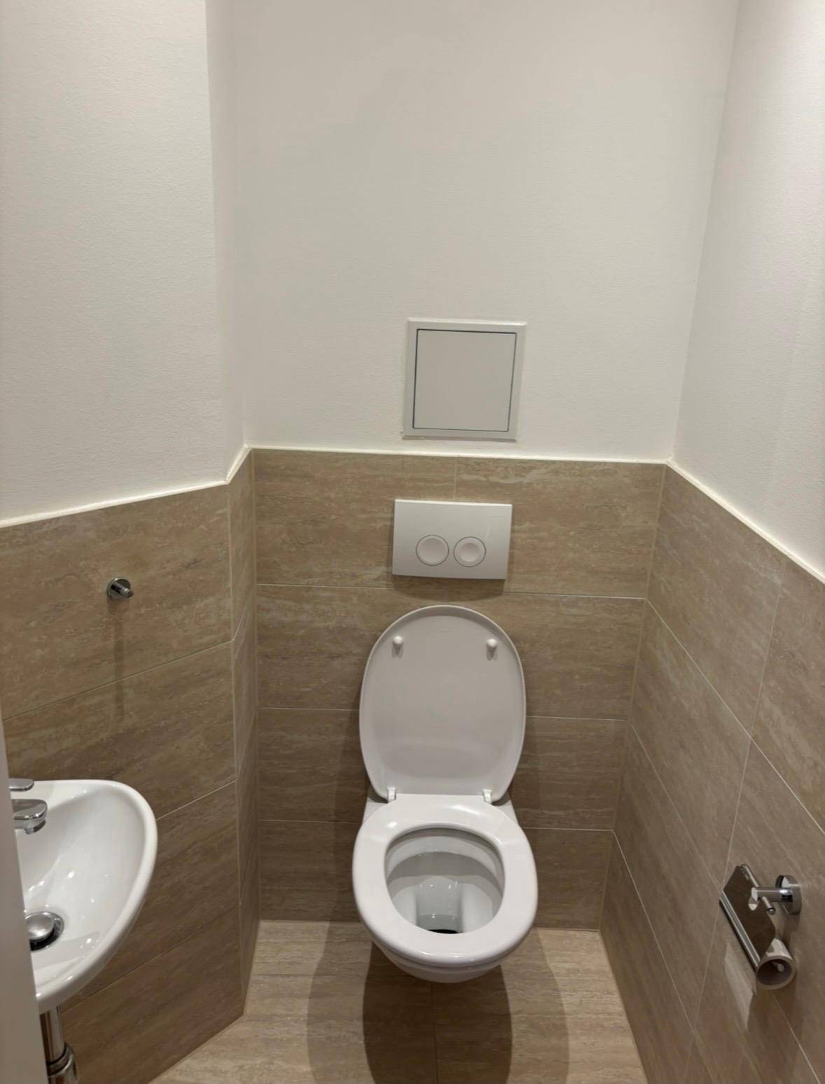 Modernes Gäste-WC mit wandhängender Toilette, kleinem Waschbecken und beigefarbenen Fliesen.