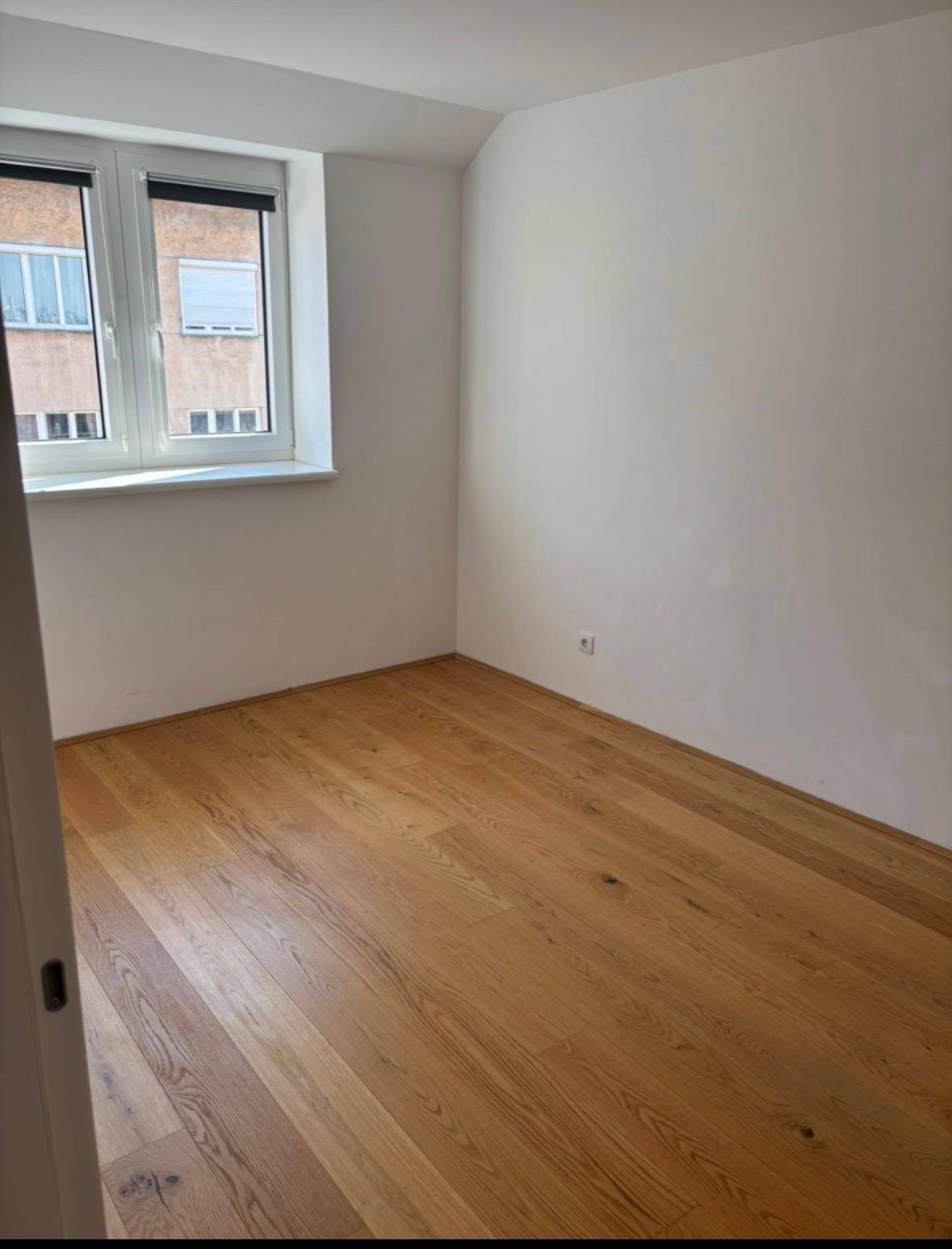 Heller Raum mit Holzboden und einem Fenster, das Tageslicht hereinlässt.