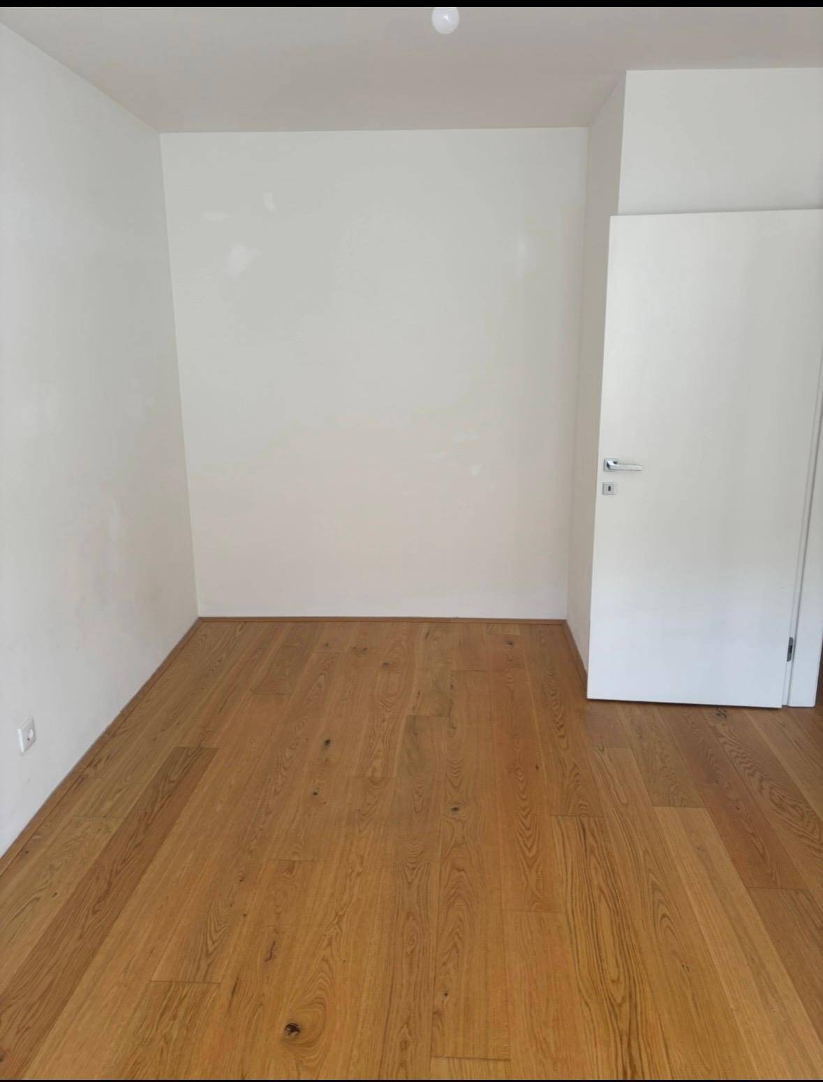 Heller, leerer Raum mit Holzboden und einer weißen Tür, bereit zur Einrichtung.