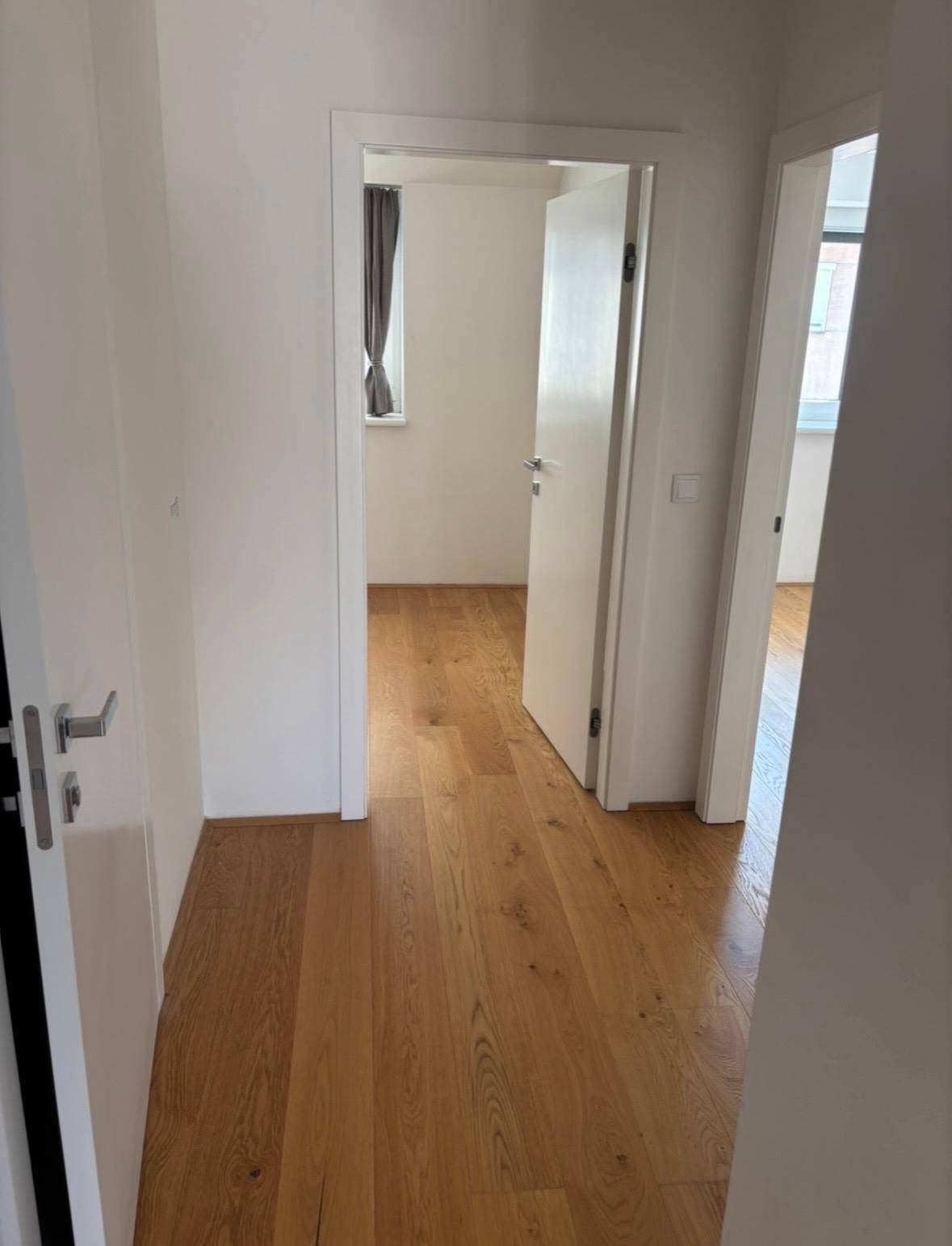 Langer Flur mit Holzboden, der zu mehreren hellen Zimmern mit weißen Türen führt.