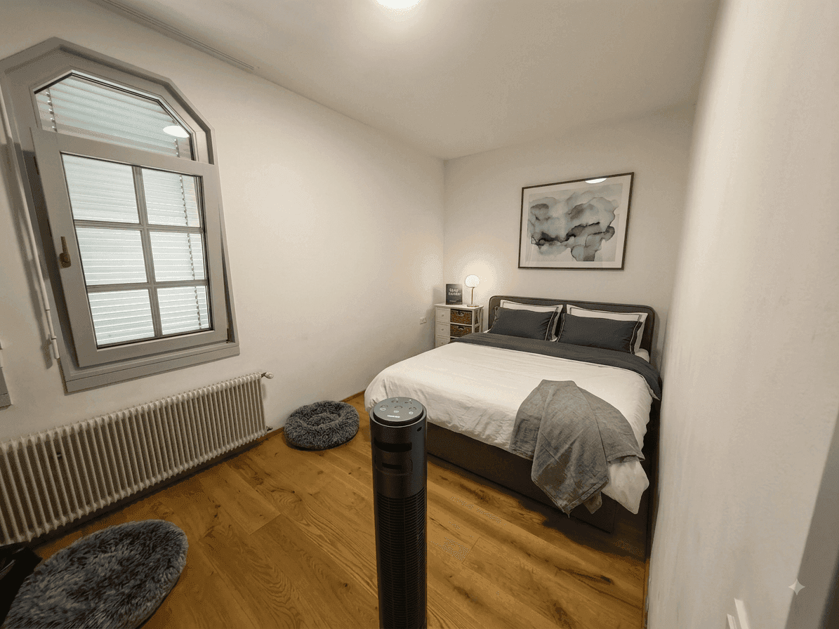 Helles Schlafzimmer mit Doppelbett, Nachttischen und einem Fenster mit Jalousien, ausgestattet mit Holzboden.