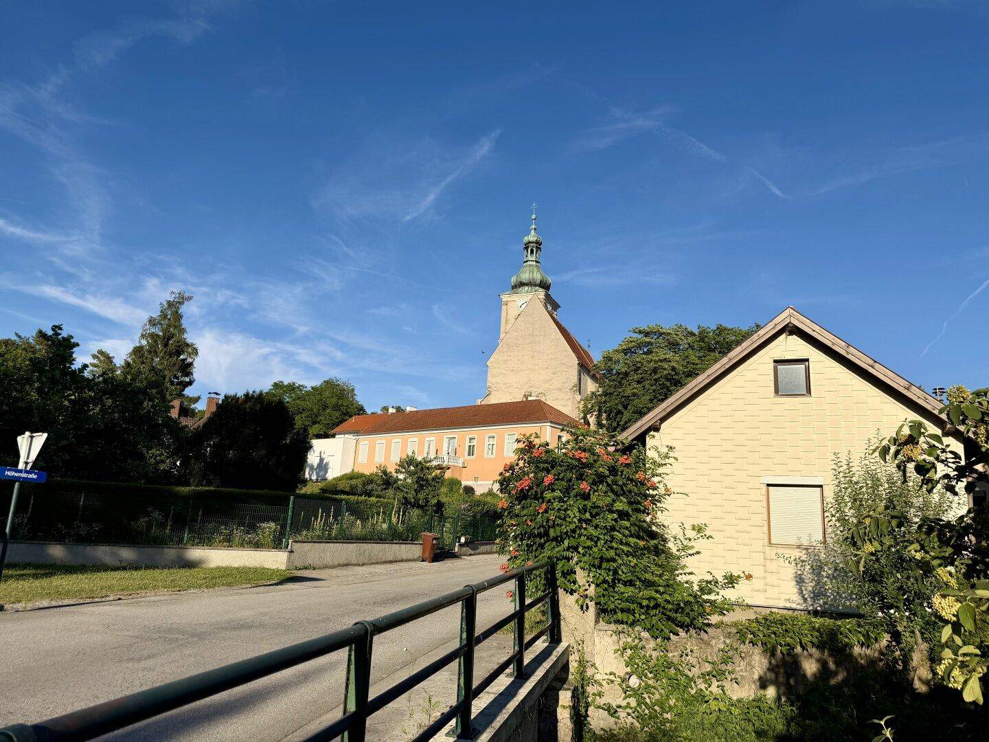 Idyllische Ansicht einer Kirche und eines Hauses mit Brücke im Vordergrund unter blauem Himmel.