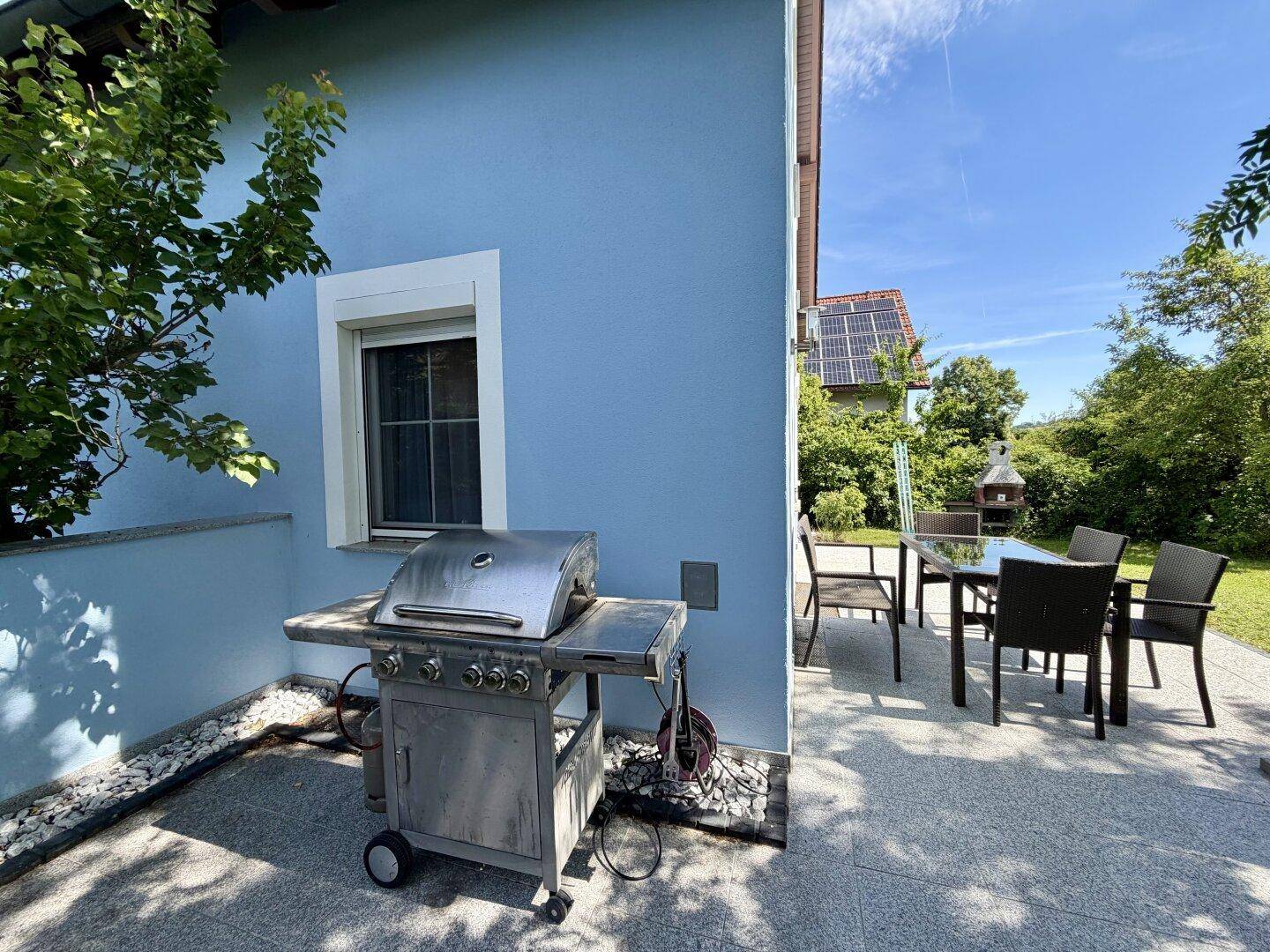 Außenbereich mit Gasgrill und Esstisch auf einer gepflasterten Terrasse, ideal für Mahlzeiten im Freien.