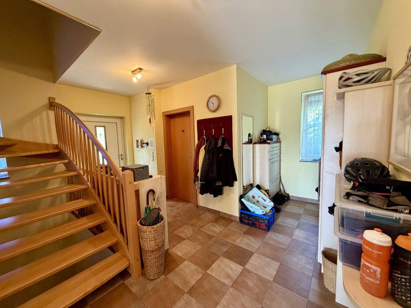 Heller Eingangsbereich mit Holztreppe, gefliestem Boden und Garderobe.