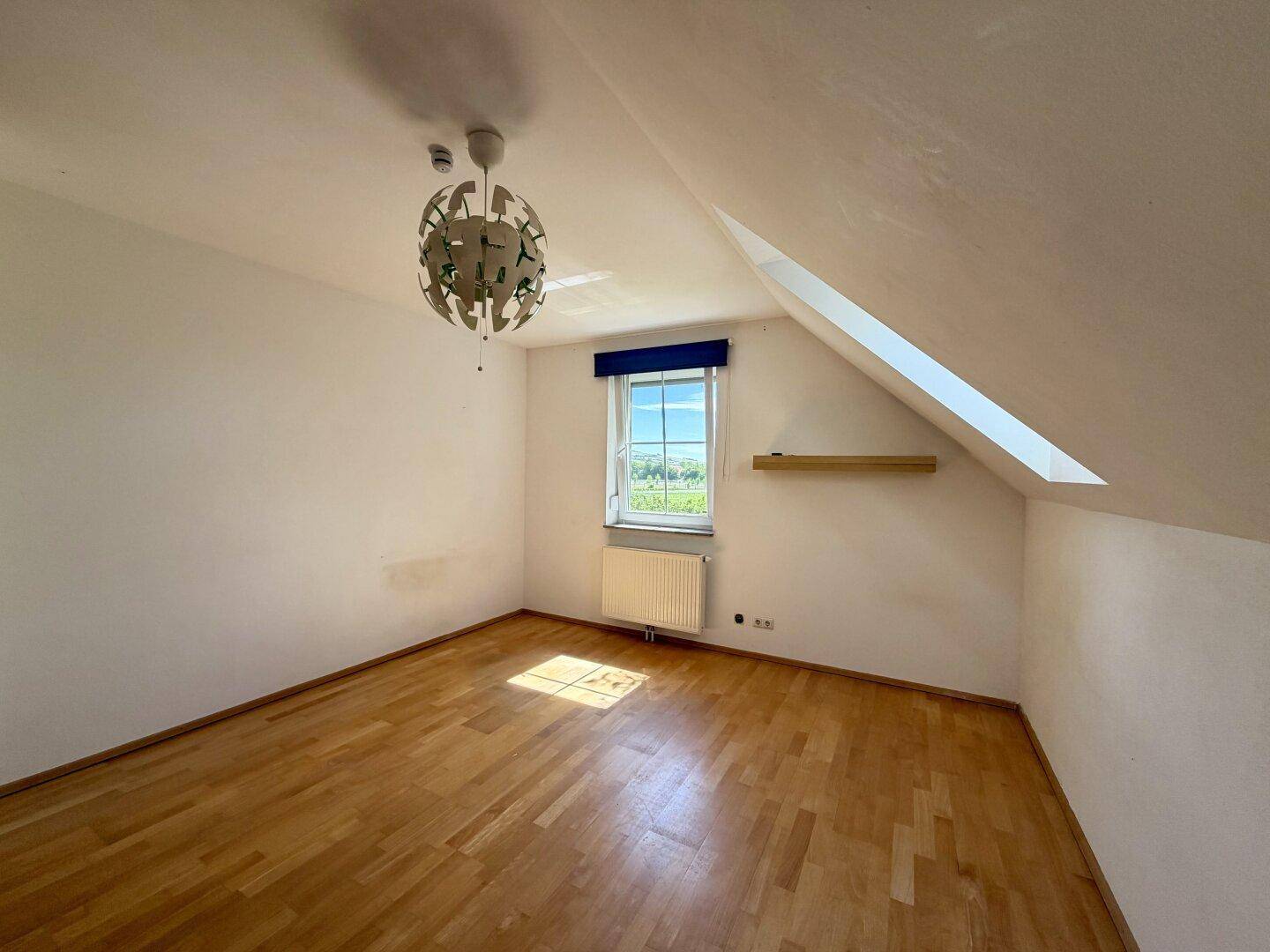 Helles Schlafzimmer im Dachgeschoss mit Holzboden, schräger Decke und weitem Ausblick.