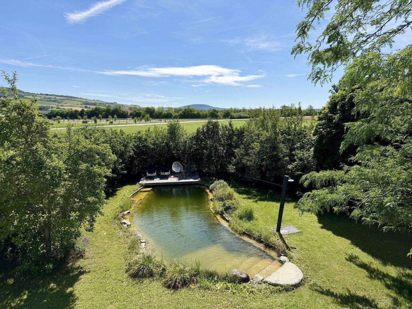 Weitläufiger Garten mit Teich und Holzdeck, umgeben von grüner Landschaft und Feldern.