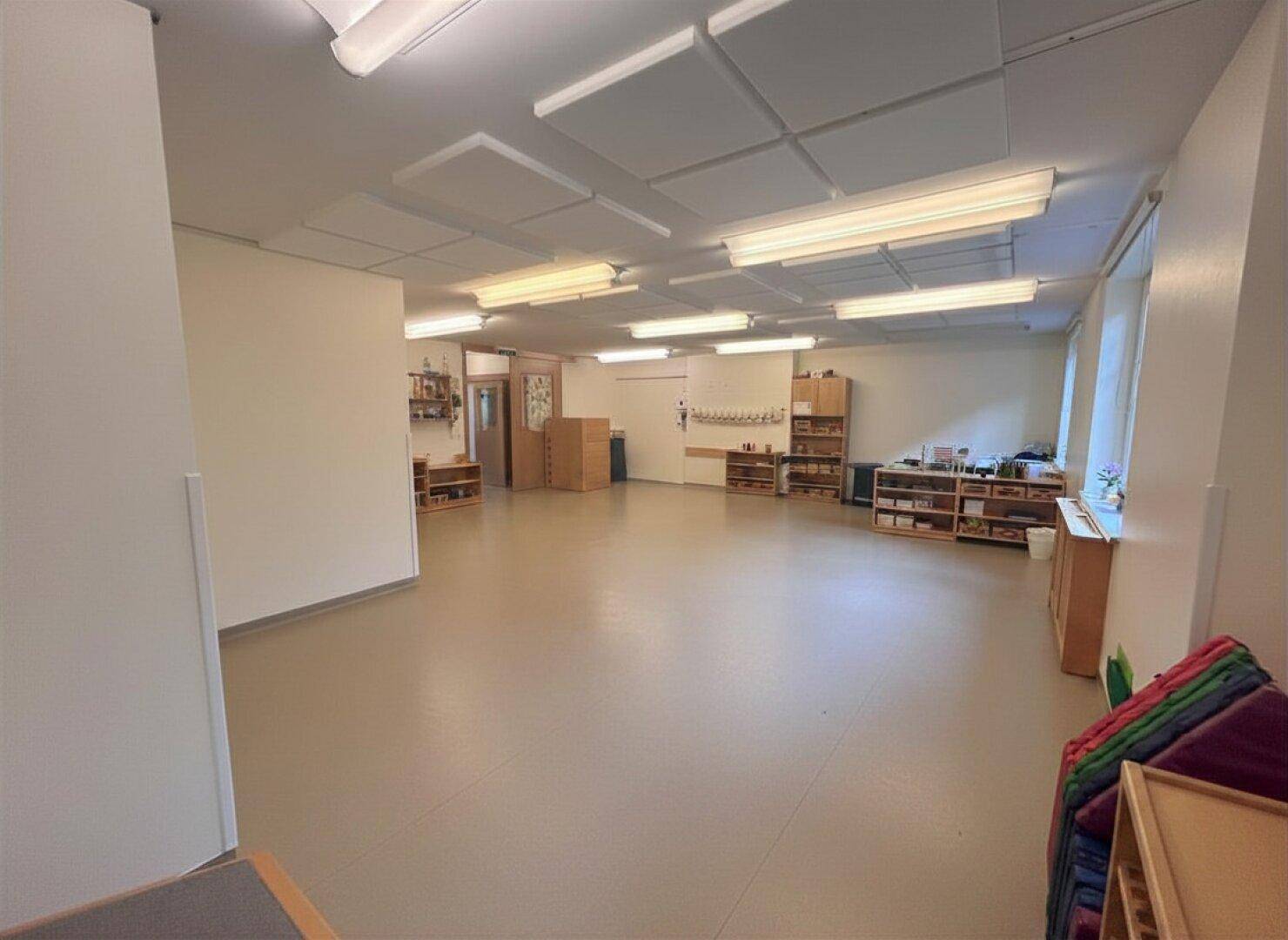 Großer, heller Raum mit Regalen und Akustikdeckenplatten, geeignet für Kinderbetreuung oder Bildungseinrichtungen.