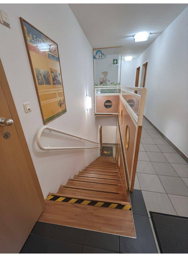 Holztreppe mit Handläufen und einem gefliesten Flur, der zu weiteren Räumen führt, mit kindgerechter Dekoration.