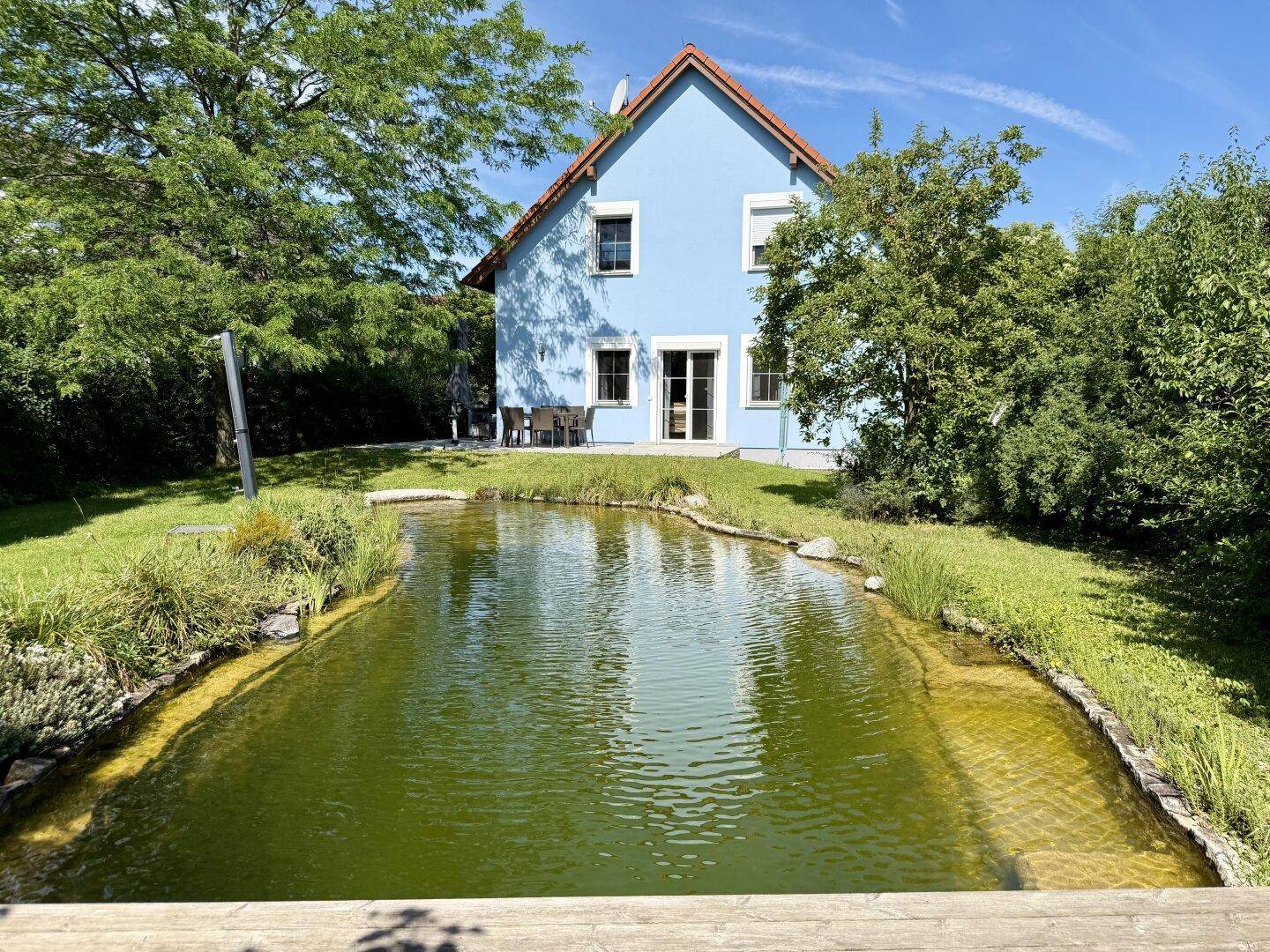 Charmantes blaues Haus mit rotem Dach, idyllisch gelegen an einem natürlichen Gartenteich.