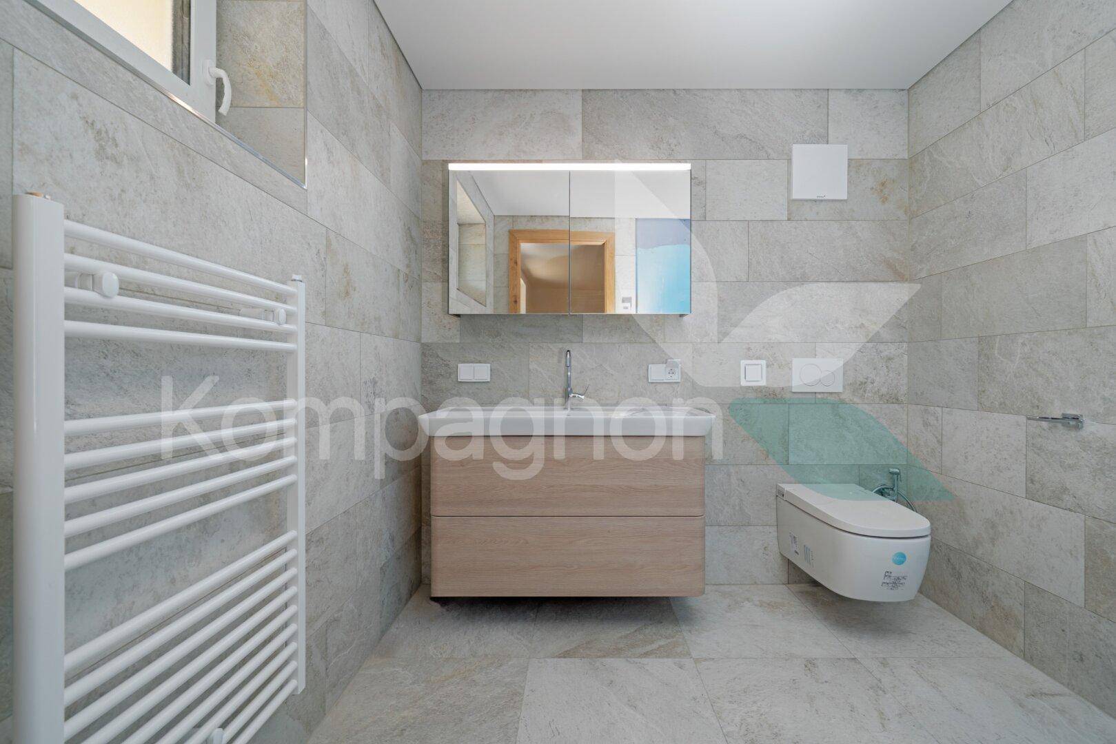 Modernes Badezimmer mit hellgrauen Fliesen, Holzwaschtisch und wandhängendem Bidet.